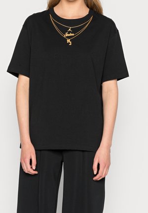Persona che indossa una maglietta nera con un design stampato di una collana dorata con il logo Jordan e le iniziali MJ.