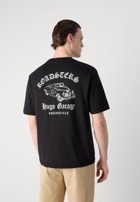 Black crew neck T-shirt made of cotton, featuring white graphic text and an illustration of a vintage car on the back.