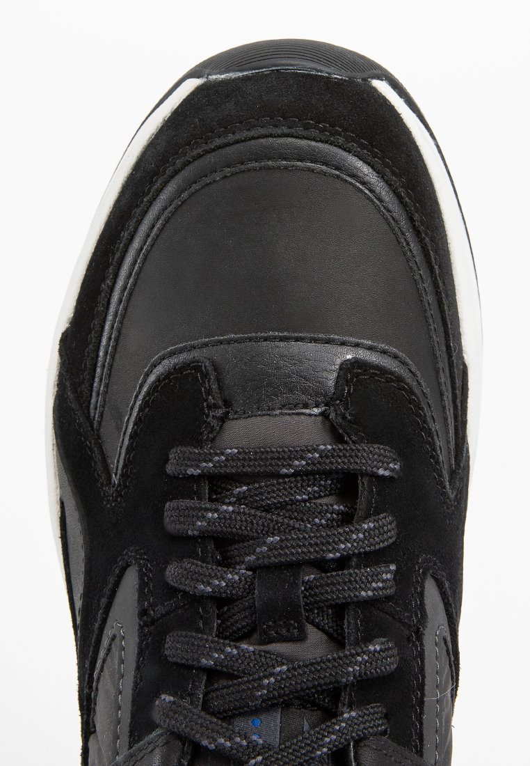 Schwarzer Sneaker aus einer Kombination von glattem Leder und schwarzem Wildleder. Er hat eine runde Schuhspitze, strukturierte Schnürsenkel und eine weiße Gummisohle.