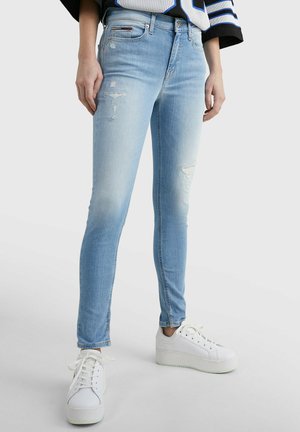 Hellblaue, enge Jeans aus Denim mit einem ausgewaschenen Design, das verblasste Stellen und kleine Risse aufweist, kombiniert mit weißen Plateausneakers.