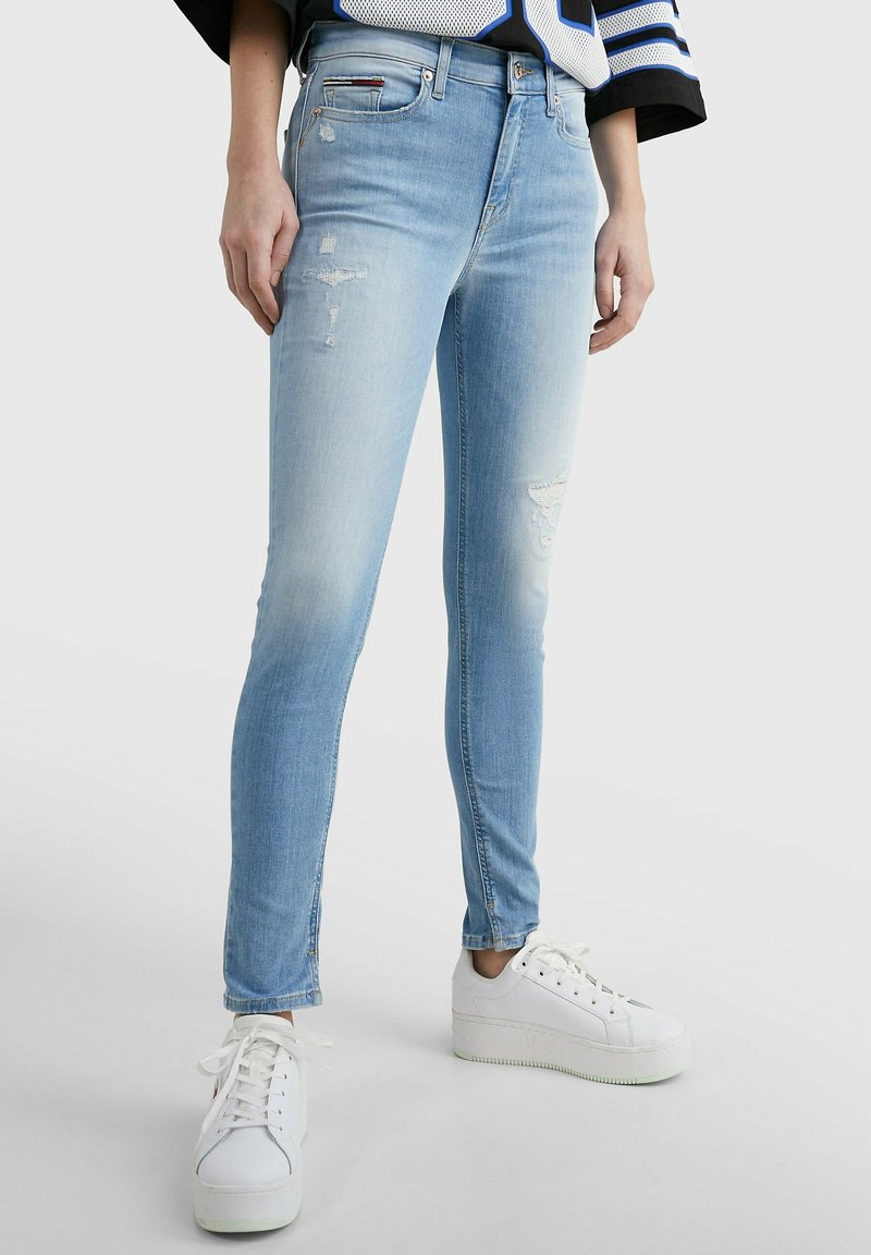 Jeans ajustados de un azul claro hechos de denim, con un diseño desgastado que presenta decoloraciones y pequeños desgarros, combinados con zapatillas deportivas blancas de plataforma.