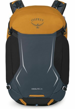 Mochila compacta de senderismo en amarillo mostaza, gris oscuro y negro con correas acolchadas, detalles reflectantes y el logo de Osprey en la parte superior.