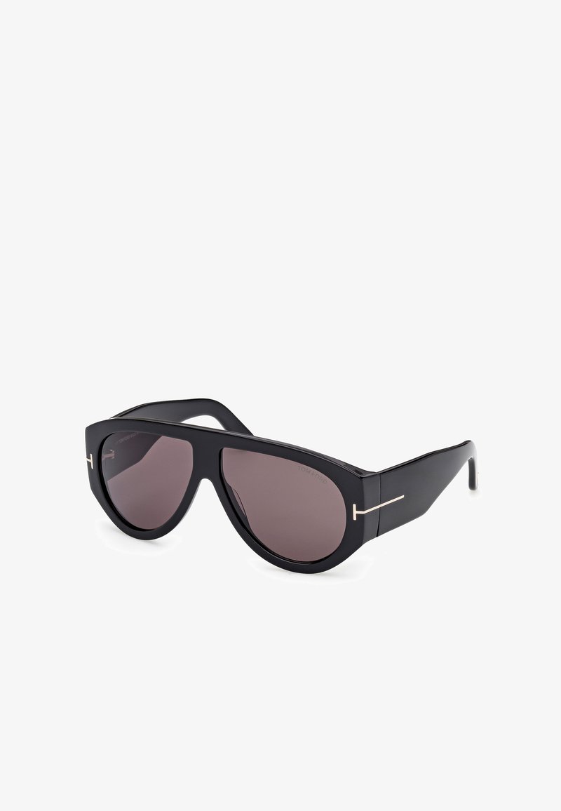 Mustad suurte mustade prillide objektiivid, millel on tumedad gradatsioonid, nurkadega raami disain ja kuldne aksentdetail tempelitel.