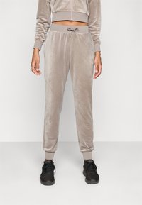 Lys beige velour joggebukser med elastisk midje og snor. Slim-fit design med ribbestrikkede ankelmanchetter. Kombinert med svarte joggesko.