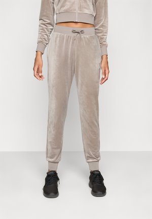 Lichtbeige velours joggers met een elastische tailleband en een trekkoord. Slim-fit ontwerp met geribbelde enkelmanchetten. Gecombineerd met zwarte sneakers.