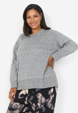 Pull en tricot gris clair à col rond, avec un ourlet côtelé et des manches longues ; associé à un pantalon sombre à motifs avec des formes abstraites.