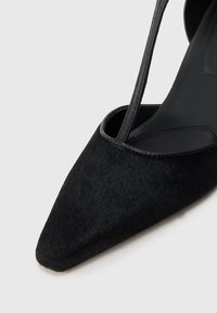 Melnas uz galu norādītas stiletto kurpes, kas izgatavotas no teksturēta materiāla ar elegantu dizainu. Iezīmējas ar plānu siksniņu un gludu iekšējo zoli.