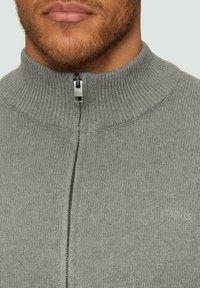 Grauer Reißverschluss-Pullover mit geripptem Kragen und weicher Textur, ausgestattet mit einem metallischen Reißverschluss, dezentem Branding und einer taillierten Passform.