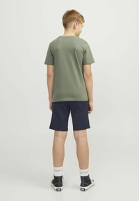 Camiseta de manga corta verde claro combinada con pantalones cortos azul marino, material de algodón, diseño casual, llevada con zapatillas altas y calcetines blancos.