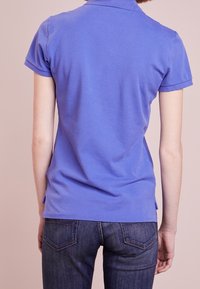 Lila bomullspiké med korta ärmar, med en ribbad krage och sidslitsar, i kombination med blå denimjeans.