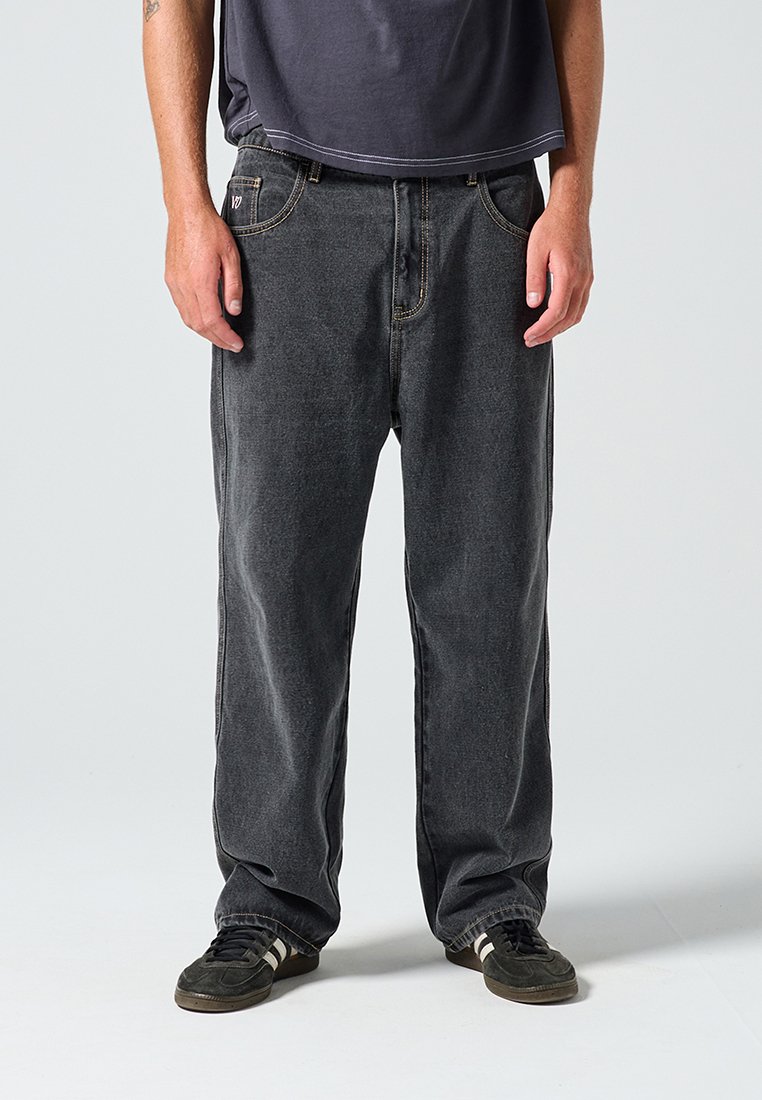 Μαύρο τζιν με φαρδιά εφαρμογή, με κανονικές τσέπες και κεντήματα σε αντίθετο κίτρινο χρώμα. Συνδυασμένο με μαύρα αθλητικά παπούτσια με λευκές ρίγες.