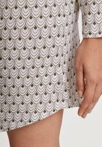 Abito a maniche corte con sfondo bianco e motivo a scallop verde oliva ripetuto. Presenta un orlo dritto e uno spacco laterale.