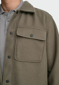 Veste en mélange de laine vert olive avec un col pointu, une fermeture à boutons et une grande poche poitrine. Les détails en métal noir mat soulignent le design.