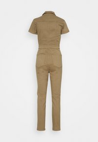 Tan jumpsuit med krage, korta ärmar, figursydd midja och raka ben. Har två bakfickor och synliga sömnadsdetaljer.