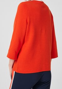 Pull orange texturé avec manches trois-quarts, encolure ronde et coupe décontractée. Coutures apparentes le long du dos.
