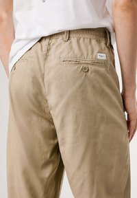 Beige Baumwollhose mit elastischem Taillenbund, zwei Gesäßtaschen und einem Logo-Tag. Weiche Textur mit lässiger Passform.