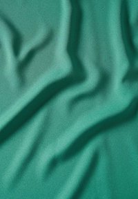 Tissu turquoise lisse avec de doux plis et des ombres légères créant une surface texturée et fluide.