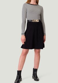 Schwarzer Rock mit weit ausgestellt Design, kombiniert mit einem Langarmtop mit einem schwarz-weißen geometrischen Muster. Schwarze Stiefeletten mit metallischen Akzenten.