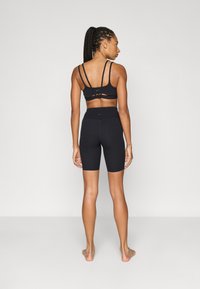 Μαύρο αθλητικό μπουστάκι με λεπτές τιράντες και σχέδιο με κοψίματα. Συνδυάζεται με εφαρμοστά μαύρα ποδηλατικά σορτς, και τα δύο από απαλό, ελαστικό ύφασμα.