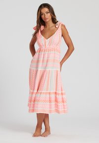 V-ringad klänning med knytband, i rosa och vit tyg som har geometriska mönster och en flerlagrig kjol. Lätt och flytande design.
