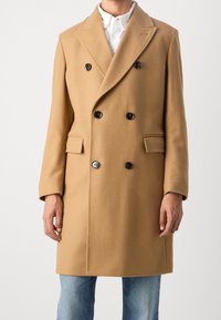 Cappotto doppiopetto in misto lana cammello, con bottoni neri, colletto a rever, tasche laterali e vestibilità sagomata.