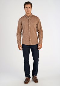 Bruine blouse met patroon en lange mouwen, voorzien van een button-down kraag, gecombineerd met marineblauwe broek en bruine schoenen met roze veters.