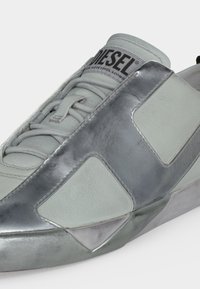 Gros plan d'une sneaker Diesel blanche et argentée avec des lacets visibles et le logo Diesel sur la languette.