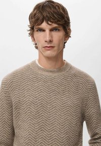 Maglione beige lavorato a maglia con motivo a spina di pesce, collo tondo e finitura testurizzata. Il tessuto appare morbido e leggero.