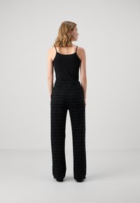 Svart topp i camisole-stil kombinert med vide bukser med et repetitivt logomønster. Glatt stoff med elastisk midjebånd. Nøytral bakgrunn.