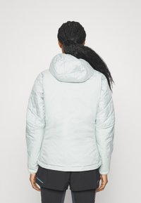 Doudoune bleu clair avec capuche, présentant une texture matelassée et des poignets élastiques, conçue pour la chaleur et le confort par temps frais.