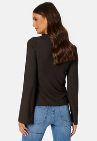 Dunkel gestreiftes Langarmtop mit weit ausgestellten Ärmeln, kombiniert mit hellblauen, figurbetonten Jeans. Der Stoff wirkt dehnbar und strukturiert.