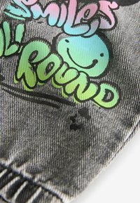 Svart denimlapp med flerfärgad text och smiley-ansikten, som inkorporerar gradienter av rosa, blått och grönt, på en texturerad tygbakgrund.