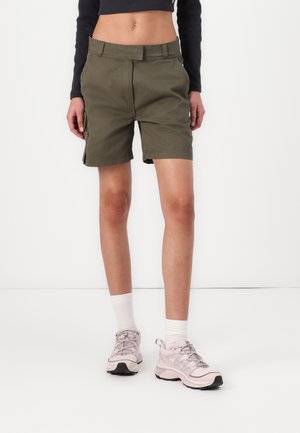 Olivgrüne Shorts mit entspannter Passform, ausgestattet mit einem klassischen Bund und Seitentaschen, kombiniert mit hellrosa Sportschuhen und weißen Socken.