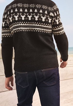 Suéter de punto negro con patrones geométricos blancos, que incluyen renos y copos de nieve, con puños y dobladillo acanalados, combinado con jeans azules.