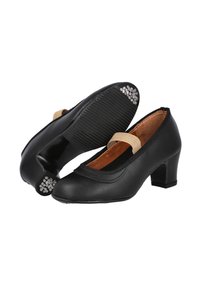 Zapatos de cuero negro con un tacón bajo, punta redonda y una correa elástica. Las suelas tienen textura con pequeños acentos metálicos.