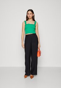 Haut court vert avec des bretelles volantées, associé à un pantalon noir ample. Accessoirisé avec un petit sac à main orange et des ballerines marron.