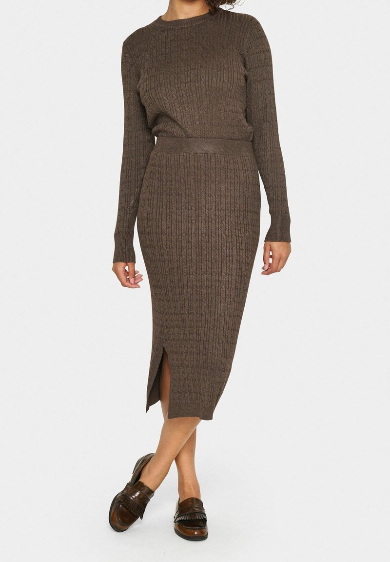 Femme portant une robe marron en maille côtelée à manches longues avec une fente sur le côté et des mocassins en cuir marron.