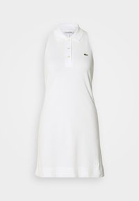 Robe polo blanche sans manches avec col et trois boutons, arborant un petit logo de crocodile vert sur la poitrine gauche.