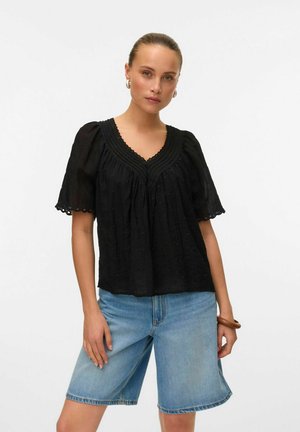 Svart kortärmad blus med V-hals, delikat spetskant, texturerad tyg och rynkad design. Matchad med blå denimshorts.