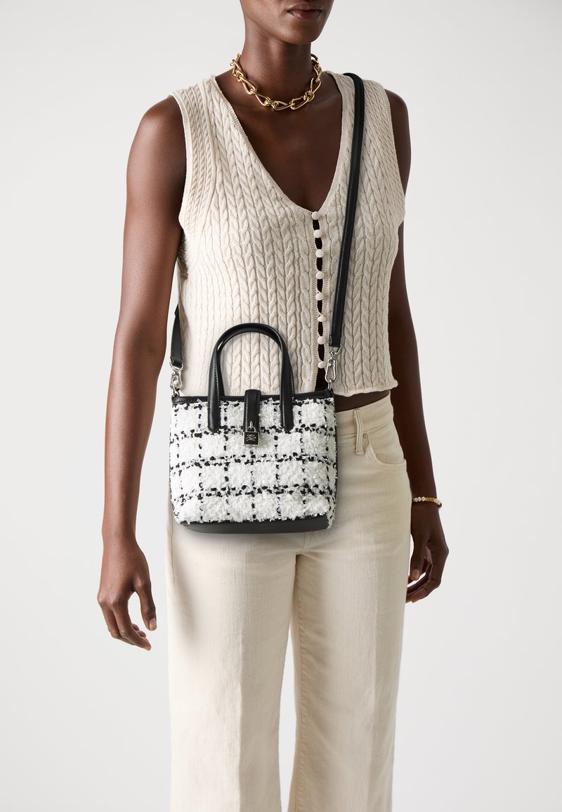 Sac à main en tweed avec des accents en cuir noir, présentant une forme structurée, des poignées supérieures et une bandoulière réglable. Motif noir et blanc.