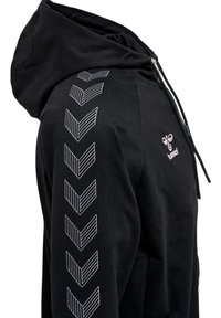 Haut à capuche noir avec une fermeture éclair à l'avant, présentant des motifs en chevron blancs le long d'une manche et un petit logo sur la poitrine. Fabriqué en tissu doux.