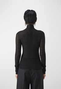 Haut noir ajusté à manches longues avec un motif en maille texturée. Col montant et poignets côtelés. Porté avec un pantalon noir ample.