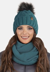 Căciulă tricotată de culoare verde-mentă, cu un model grozav și o pompon din blană artificială în vârf, asortată cu o fular infinity texturat.