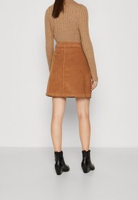 Faldita de pana marrón con un diseño ligeramente acampanado, hasta la rodilla. Combinada con una blusa marrón de canalé y botas negras hasta el tobillo.