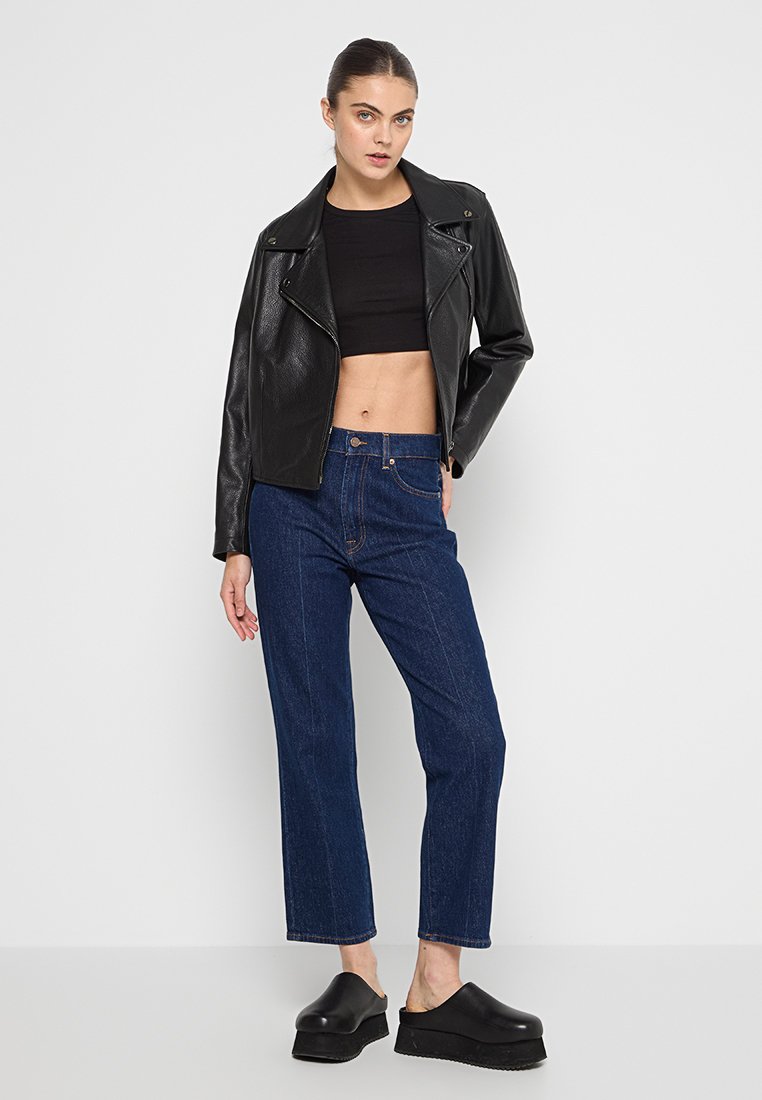Veste en cuir noir de motard, haut noir court, jean droit bleu et chaussures noires à plateforme. Conception simple, texturée et ajustée.