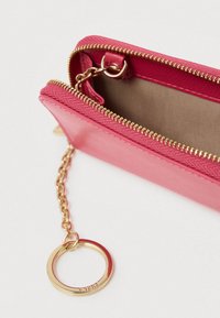 Rozā maks ar teksturētu virsmu, zelta rāvējslēdzēju un ķēdi. Iekšpuse ir bēša. Aprīkots ar zelta atslēgu riņķa stiprinājumu ērtai nēsāšanai.