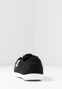 Black canvas sneaker with a low profile and white rubber sole. Features a rounded toe and subtle stitching details. Brand logo on heel.