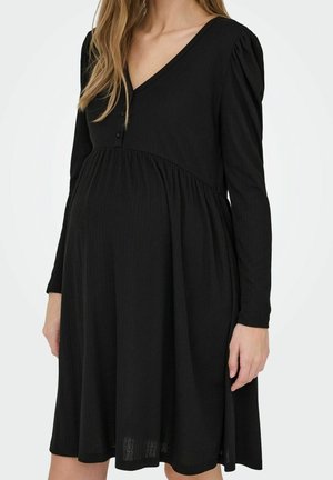 Kobieta w ciąży nosząca czarną sukienkę ciążową z długim rękawem, dekoltem w serek i marszczonymi detalami w talii.