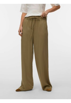 Persoană care poartă pantaloni largi kaki, cu talie cu șnur, și pantofi maro, pe un fundal simplu.