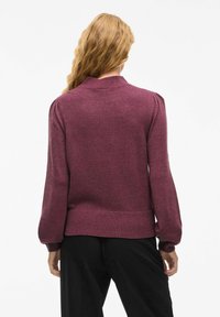 Pull en maille bordeaux avec col, manches bouffantes, poignets et ourlet côtelés, présentant une texture lisse et une coupe décontractée.